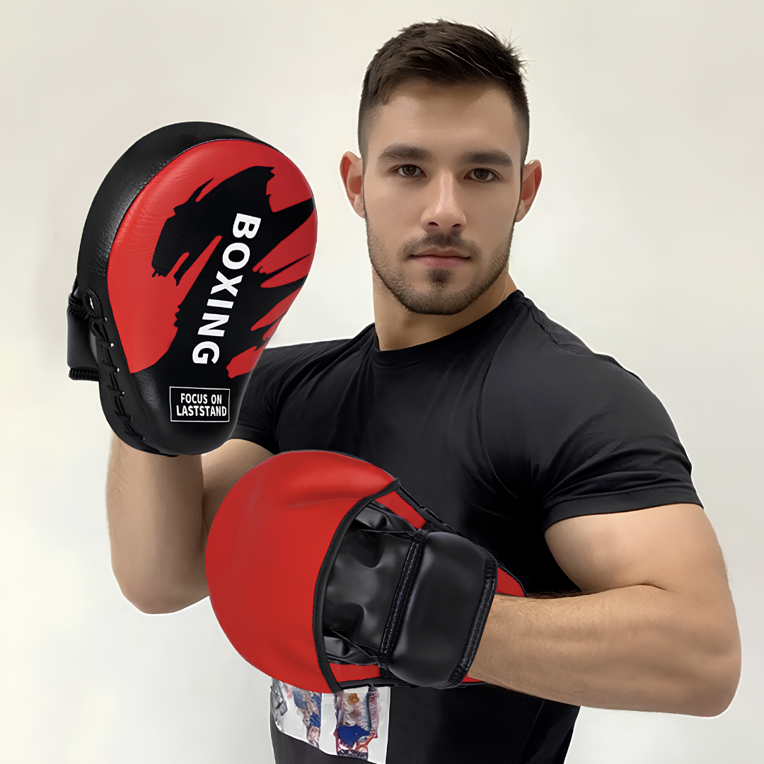 Mann mit roten und schwarzen Box-Pratzen, demonstriert den Einsatz beim Training, ideal für Kampfsportarten wie Boxen oder Muay Thai.